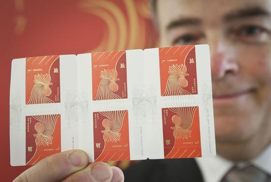 1月9日，在加拿大温哥华，一名工作人员展示中国鸡年生肖国际版邮资邮票。